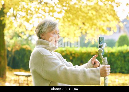 Outdoor portrait of happy and active mature woman recording herself with phone, social media and vlogging concept Stock Photo
