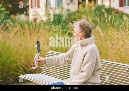 Outdoor-Porträt einer glücklichen und aktiven Reifen Frau, die sich mit Telefon, sozialen Medien und Vlogging-Konzept aufnimmt Stockfoto