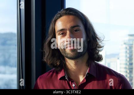 Kopfaufnahme eines jungen latinos, der in die Kamera schaut und im Büro lächelt. Stockfoto