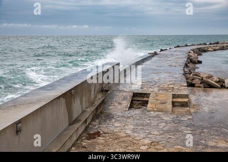 Dramatische Meereswellen plätschern bei stürmischem Wetter gegen Steinbruch und Betonmauer. Küstenschutzinfrastruktur in Novigrad, Istrien, Stockfoto