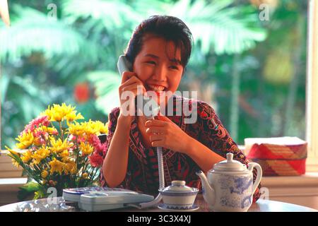 Singapur. Junge Frau zu Hause, die am Telefon spricht. Stockfoto