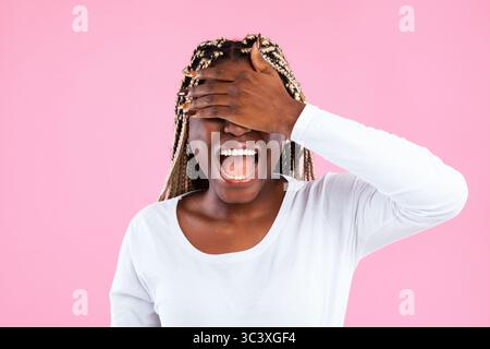 Glückliche junge afroamerikanische Frau, die ihre Augen mit der Hand bedeckt Stockfoto