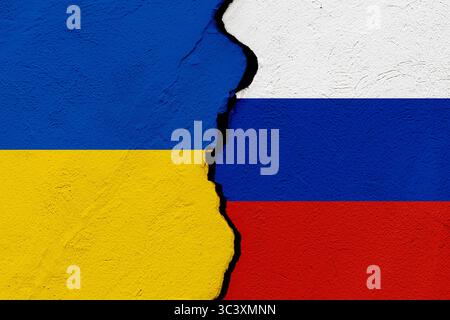 Die Fahnen der Ukraine und der Russischen Föderation in eine zerrissene Mauer. Geopolitik und Kriegskonzept Stockfoto