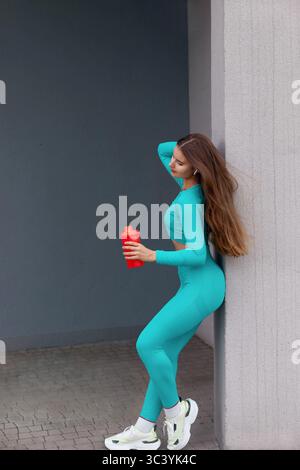 Schöne Läuferin stehen draußen halten Wasser aus der Flasche. Fitness Frau eine Pause nach dem Lauftraining. Stockfoto