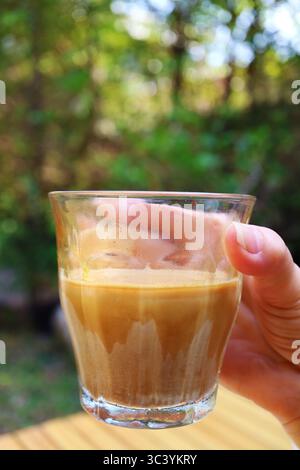 Nahaufnahme eines Glases mit schmutzigem Latte-Kaffee in der Hand Stockfoto