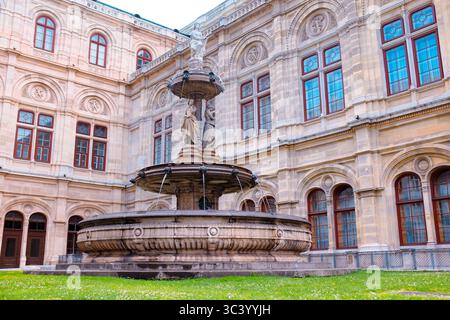 Brunnen im Innenhof der Wiener Staatsoper, umgeben von kunstvoller Renaissance-Architektur und historischen Fenstern an einem Sommernachmittag. Stockfoto