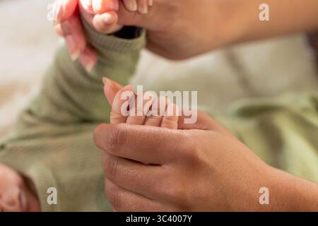 Afroamerikanische Mutter, die die Hand der Säuglingstochter in grünem Rippelanzug am Bettzeug hält Stockfoto