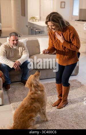 Paare trainieren Golden Retriever auf Teppich im Wohnzimmer mit Hundeschlitten während der Sitzung Stockfoto
