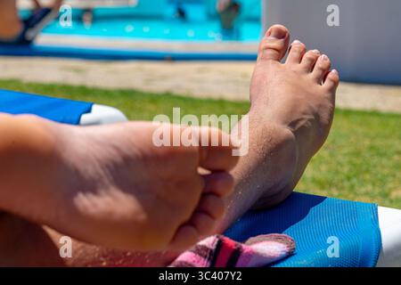 Schöne Füße des weißen kaukasischen Mannes, der sich am schönen Sommertag im Badebereich des Schwimmbades entspannt Stockfoto