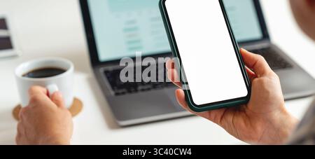 Modell eines Smartphones mit weißem, leerem Bildschirm in der Hand einer Geschäftsfrau vor dem Hintergrund eines Laptops auf dem Tisch Stockfoto