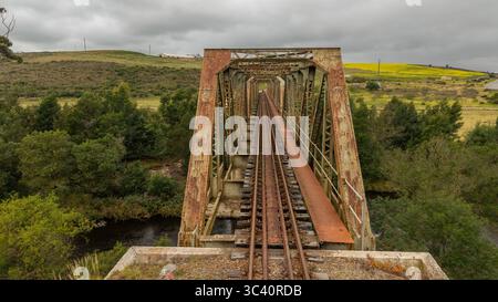 Aus der Vogelperspektive der rostigen Eisenbrücke, die durch üppiges Grün führt und sich in den dunklen Gewässern darunter spiegelt, Riversdale, Westkap, Südafrika. Stockfoto