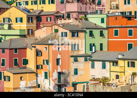 Sonnenlicht trifft auf die abgenutzten Pastellfassaden der Boccadasse in Genua, Italien, wo sich Dächer, Rollläden und Balkone überschneiden Stockfoto