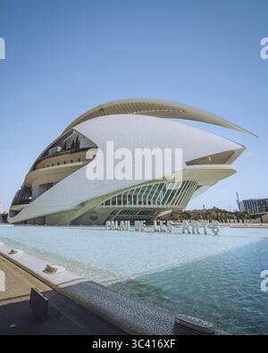 Valencia, Spanien - 16. April 2025: Blick auf den Palau de les Arts Reina Sofia schimmert im reflektierenden Pool, dessen futuristische weiße Architektur sich vom klaren blauen Himmel abhebt. Stockfoto