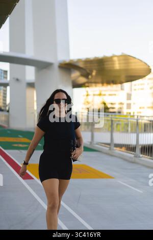 Frau geht draußen in Aktivkleidung mit Sonnenbrille an hellem Tag Stockfoto