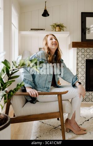 Lachende Frau, die in einem hellen, modernen Wohnzimmer sitzt Stockfoto