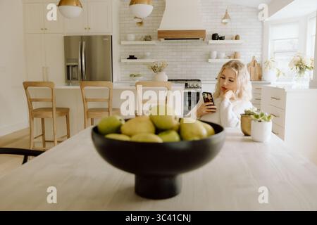 Frau mit Smartphone in der Küche in der Nähe einer Schüssel frischer Birnen Stockfoto