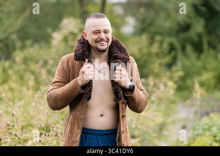 Lächelnder Mann mit offenem braunem Lammfell in einer natürlichen Umgebung im Freien, der eine entspannte Stimmung und Verbindung mit der Natur zeigt. Perfekt für das Leben Stockfoto