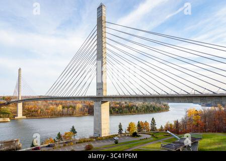 Betonhängebrücke über einen großen Fluss mit bewaldeten Ufern auf dem Gipfel der Herbstfioliage Stockfoto