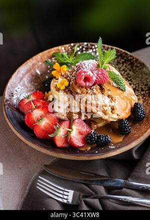 Ein Stapel köstlicher Pfannkuchen mit Schlagsahne und frischen Beeren, wunderschön mit Früchten dekoriert. Leckeres hausgemachtes Frühstück. Stockfoto
