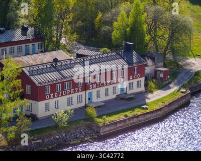 Das alte Industriegebäude Oxdjupets Snickerier, Vaxholm Socken, in der Nähe von Stockholm Schweden von einem hohen Aussichtspunkt an der Küste mit Bäumen dahinter Stockfoto