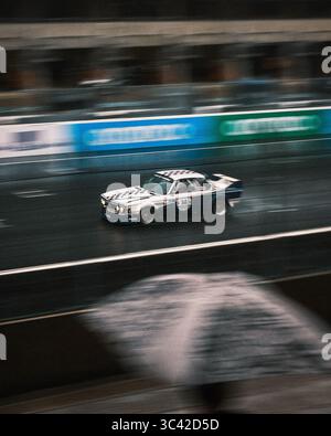 Le Mans, Frankreich - 07. Juni 2025: Blick auf einen Oldtimer, der am legendären Place Luigi Chinetti vorbeifährt, unter einem trostlosen Himmel, verschwimmt durch Bewegung und Regen. Stockfoto