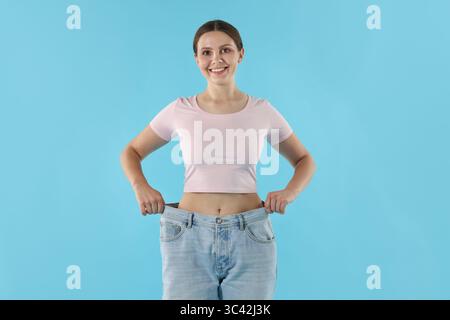 Schöne Frau, die alte Jeans nach Gewichtsverlust auf hellblauem Hintergrund trägt Stockfoto