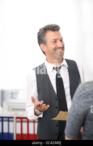 Mann im Anzug, der mit der Frau im Büro spricht, lächelt Stockfoto