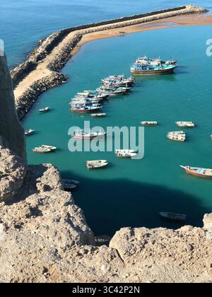 Blick aus der Vogelperspektive auf Fischerboote, die in einem ruhigen Hafen mit einem Steinbruch an der iranischen Küste ankern. Stockfoto