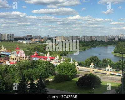 Ein lebhafter Blick aus der Luft auf einen farbenfrohen Vergnügungspark, eingebettet von einem ruhigen Fluss, mit dem Stadtbild von Moskau, Russland, unter einem teilweise bewölkten Himmel. Stockfoto