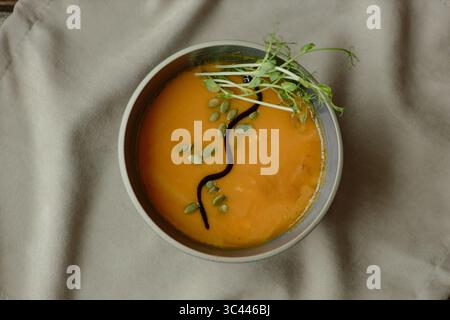 Schüssel Kürbissuppe garniert mit Kürbissamen und Microgreens Overhead Stockfoto