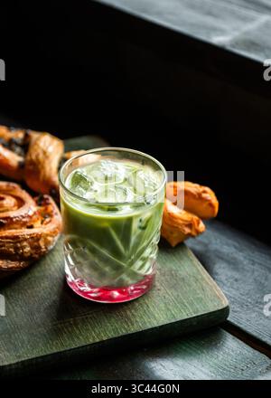 Erfrischender Erdbeermatcha Latte serviert mit verschiedenen Backwaren auf einem Holzbrett auf einem rustikalen Tisch. Gemütliche und einladende Einrichtung im Café-Stil Stockfoto