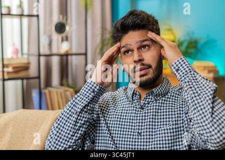 Kranker, kranker indischer Mann, der Schläfen reibt, um Kopfschmerzen zu heilen, leidet unter Spannung und Migräne, Stress, grimmige Schmerzen, Bluthochdruck zu Hause. Der Hindu-Typ drinnen auf der Couch. Lifestyle Stockfoto