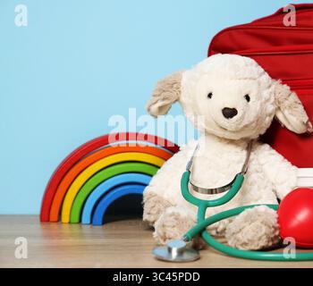 Kinderärztliches Konzept. Spielzeug, Stethoskop und erste-Hilfe-Set auf Holztisch vor hellblauem Hintergrund, Nahaufnahme Stockfoto