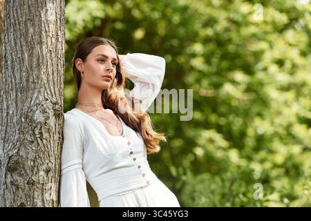 Eine strahlende Frau mit fließenden Haaren lehnt sich anmutig an einen Baum und umhüllt die Schönheit der Natur. Stockfoto