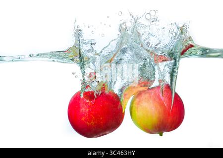 Leuchtend rote Äpfel, die in Wasser getaucht sind, erzeugen ein dynamisches Spritzen mit Blasen und Kräuseln, das Frische und Bewegung hervorhebt. Stockfoto