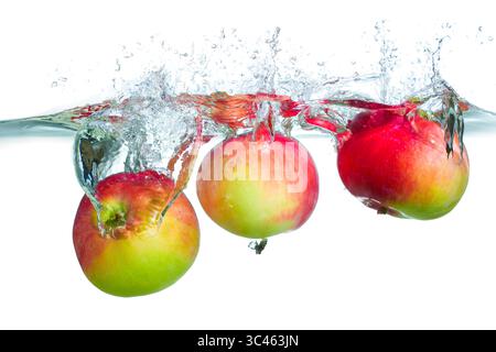 Dynamischer Spritzer frischer roter Äpfel, die in klares Wasser eindringen und Blasen und Kräuselungen für einen erfrischenden und lebendigen Effekt erzeugen. Stockfoto