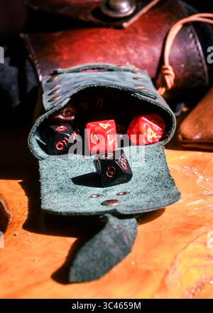 Eine Ledertasche verschüttet bunte polyedrische Würfel auf einen Holztisch, perfekt für Rollenspiele auf der Tischplatte. Stockfoto