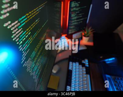 Digitales Studio mit Cyber-Codierung für Remote-Workstation mit farbenfrohen Farblichtern, Code auf dem Bildschirm und modernen Peripheriegeräten. Konzept des futuristischen Remote-Jobs, IT Stockfoto