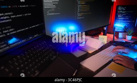 Programmierer schreibt Code über einen abgesetzten Nachtarbeitsplatz mit mehreren Bildschirmen, RGB-Beleuchtung und organisiertem, modernem Schreibtisch. Konzept der digitalen Schöpfung, Software DE Stockfoto