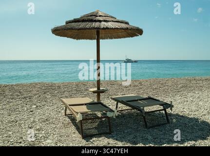 Sonnenschirm mit zwei Liegestühlen an einem heißen Sommertag in Sizilien Stockfoto