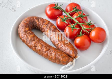 Eine einzelne Wurst und frische Tomaten, einfach auf einem hellen, sauberen Hintergrund Stockfoto