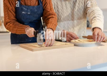 Paare, die Teig schneiden und arrangieren auf weißer Küchenarbeitsfläche mit Pizzaschneider Stockfoto