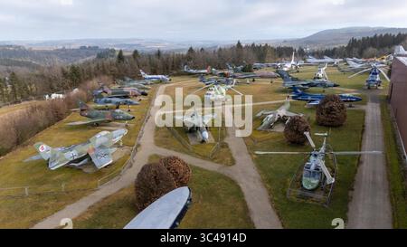 Aus der Vogelperspektive eines Flugzeugmuseums im Freien mit verschiedenen Militärflugzeugen und Hubschraubern auf grasbewachsenen Flächen, umgeben von Bäumen und Hügeln im Stockfoto