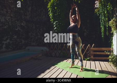 Entspannte Yoga-Session am Pool in einem grünen Garten, bei der Achtsamkeit, Wohlbefinden und Fitness im Freien im warmen Morgenlicht zum Ausdruck kommen. Stockfoto