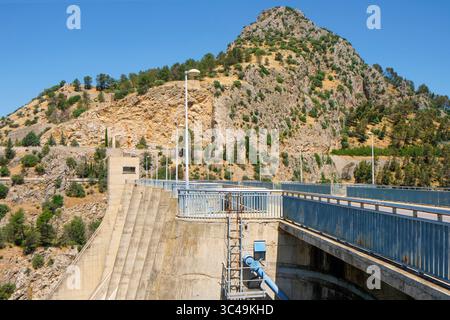 Die Betonkonstruktion des Iznajar-Staudamms erhebt sich an einem felsigen Hügel in Spanien, an dessen Basis ein Wasserkraftwerk steht, das Energie aus dem Strom fr Stockfoto