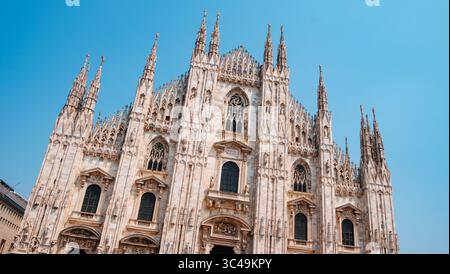 Ein klarer Blick auf die komplizierte Fassade der Mailänder Kathedrale, die von unten aufgenommen wurde und den vertikalen Aufstieg der Türme und Skulpturen vor einem wolkenlosen Su zeigt Stockfoto