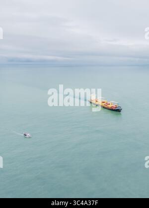 Aus der Vogelperspektive eines Frachtschiffes, das auf dem ruhigen, türkisfarbenen Wasser segelt und unter hellem Himmel eine weiße Spur hinterlässt, Batumi, Adjara, Georgia. Stockfoto