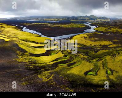 Aus der Vogelperspektive ziehen sich geflochtene Flüsse durch eine surreale Landschaft mit moosbedeckten Lavafeldern in der Nähe von Lakagígar unter einem brütenden Himmel. Kirkjubaejarklaustur Stockfoto