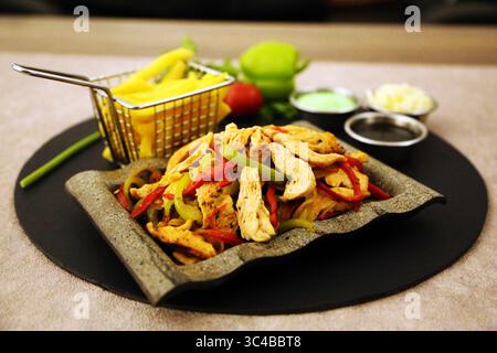 Gegrilltes Hähnchenfajita mit Paprika und Pommes Frites auf einem rustikalen Steinteller. Stockfoto