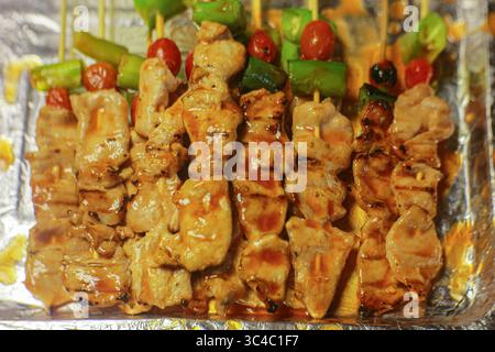 Grillspieße mit roter Sauce, Paprika und Tomaten. Thai Street Food wird auf einem Silbertablett auf einem Nachtmarkt ausgestellt. Stockfoto